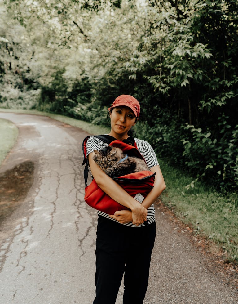 Femme marchant avec un chat dans un sac le long d’un chemin pittoresque à Toronto, entourée par la nature.