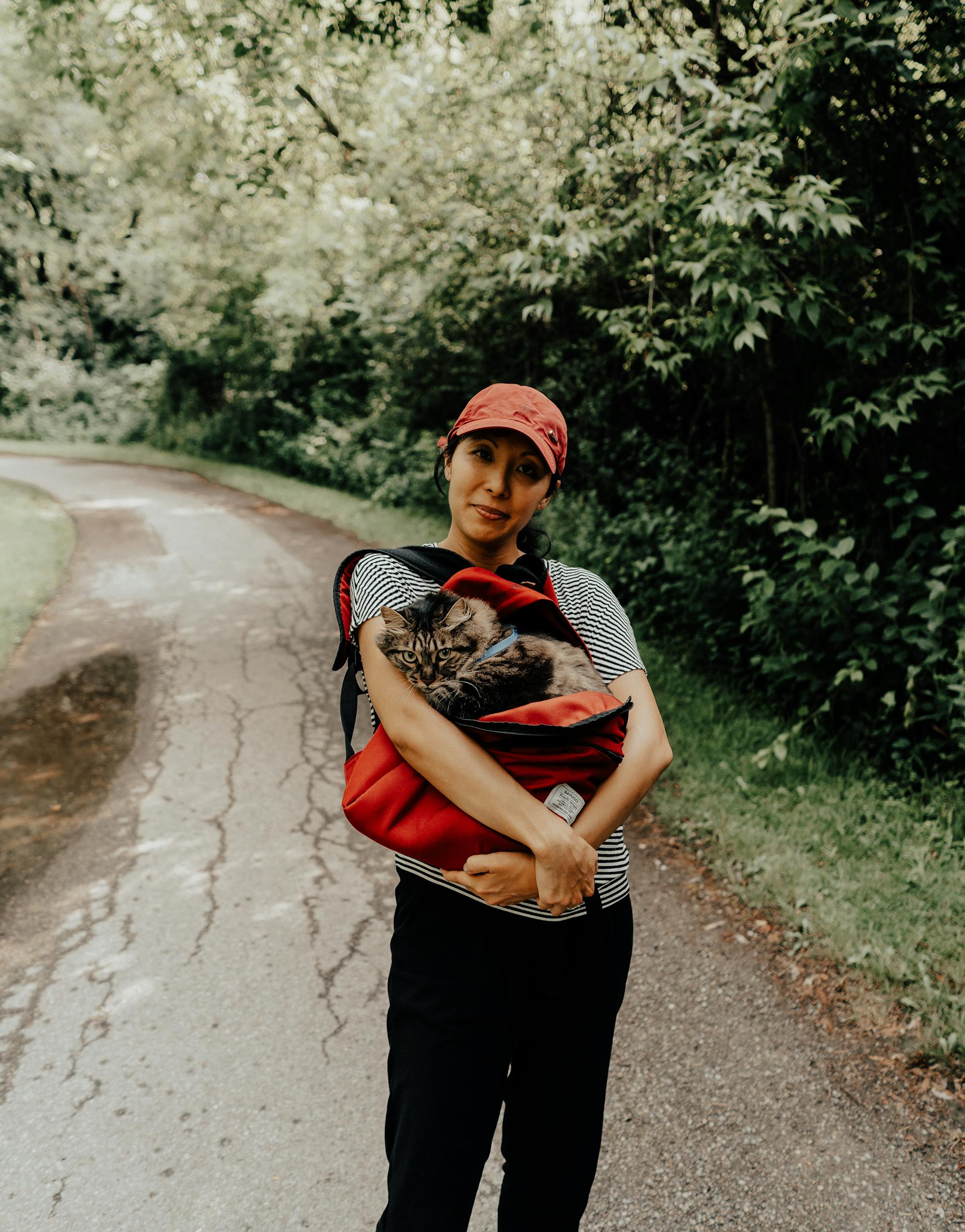 Femme marchant avec un chat dans un sac le long d’un chemin pittoresque à Toronto, entourée par la nature.